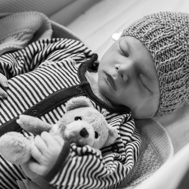 Sleeping baby wearing a knitted hat and cuddling a teddy bear dressed in a striped suit